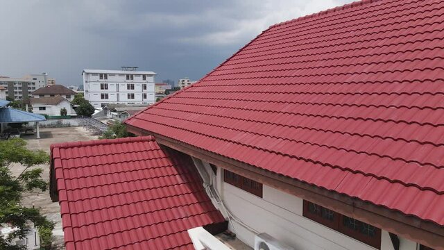 Red brown hacienda concrete roof tiles on big isolated house with suburban-scapes, residential buildings, and cloudy rainy sky in the backdrop. City village house in Southeast Asia.