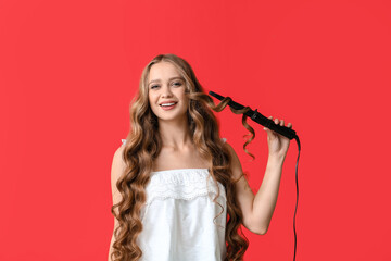 Beautiful young woman with curling iron for hair against color background