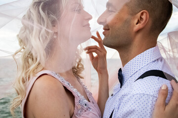 Creative hipster wedding by the sea. The bride is in a pink dress and veil, the groom is in beautiful trousers with suspenders and a youth shirt. Madness, fun and an unusual approach to marriage