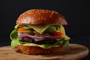 Homemade burger with grilled beef, cheese, onion, tomato, and green salad, sauce, with pickles and French fries,and a glass of beer in the background.