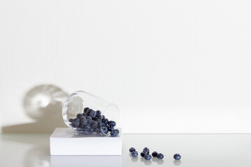 Blueberries in a glass on a white glass table, white wall background. Berries in a glass. Shadows on the wall. Vegetarian and organic food concept.