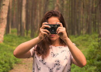 Cheerful girl takes pictures of the beauty of the forest with a retro camera