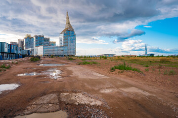 Multi-storey buildings under construction with an unfinished spire on the background of a muddy road