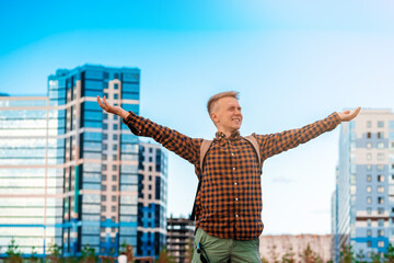 Fototapeta na wymiar A happy young man in a checked shirt spread his arms in the sky against the background of multi-colored multi-storey new buildings, happiness from buying real estate