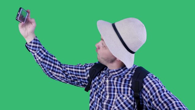 Young funny tourist in hat taking selfie on isolated green background. Travel, tourism, hike, technology and people concept
