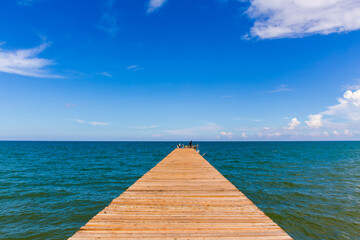 Obraz na płótnie Canvas Wooden bridge extending into the sea with Deep Blue ocean sky clouds. Landscape with Ocean small waves water reflection copy space for text. Illustration for tourism, website or ad. Andaman sea.