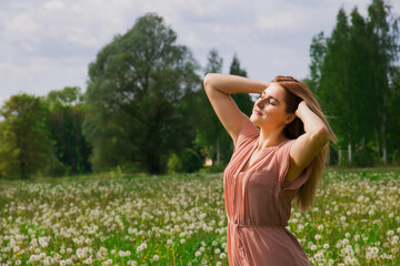 Naklejka na ściany i meble Young happy woman with her arms wide spread enjoys in the summer flower meadow white dandelions