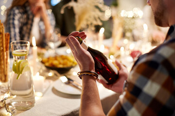 holidays and celebration concept - happy friends having christmas dinner at home with bottle of non-alcoholic red wine