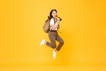 Fototapeta na wymiar Young pretty Asian woman tourist backpacker smiling and jumping with camera in hand isolated on yellow background