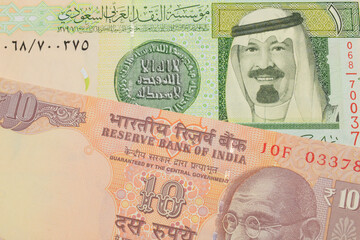 A macro image of a orange ten rupee bill from India paired up with a green and yellow one riyal...