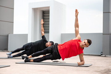 Group of athletic men doing side plank workout exercise outdoors on rooftop floor