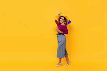 Full length portrait of happy young attractive African American woman raising shopping bags and holding mobile phone in isolated studio yellow background