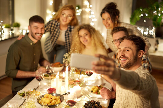 holidays, celebration and people concept - happy friends taking selfie with smartphone at home christmas dinner party