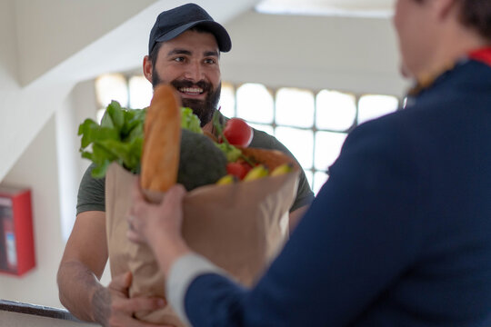 Delivery Man With Beard And Express Grocery Delivery Service. Man In Green Shirt With Paper Bag That He Just Bring To Middle Age Woman.