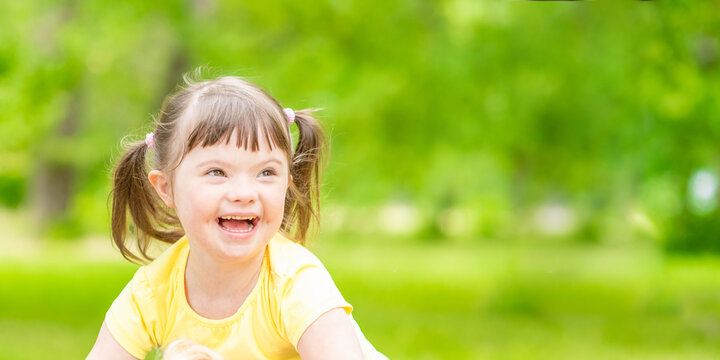 Portrait of a joyful little girl with syndrome down in a summer park. Empty space for text