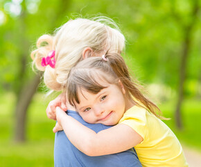Happy little girl with syndrom down hugs mother in a summer park