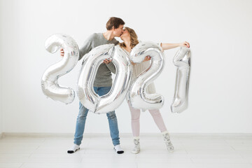 Holidays, festive and party concept - Happy loving couple holds silver 2021 balloons on white background. New Year celebration.