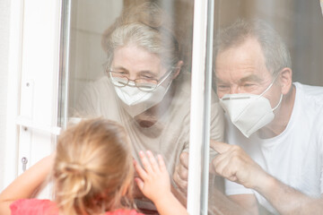 Granddaughter communicates with her grandparents through a transparent door during the coronavirus epidemic