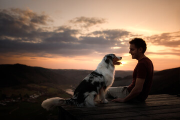 A man with a dog at sunset. walk with a pet. Australian Shepherd and owner in nature look at a beautiful view 