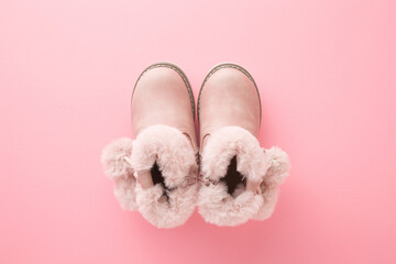 Leather warm baby boots on light pink table background. Pastel color. Closeup. Top down view.