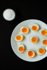 Homemade Unami Soy Sauce Eggs on a white plate on a black background, top view. Overhead, from above, flat lay.
