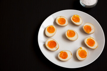 Homemade Unami Soy Sauce Eggs on a white plate on a black background, side view. Copy space.