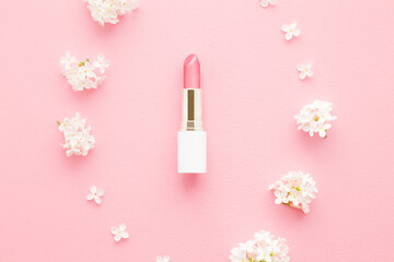 Pink lipstick in white tube in circle middle of fresh lilac blossoms on light pastel table...