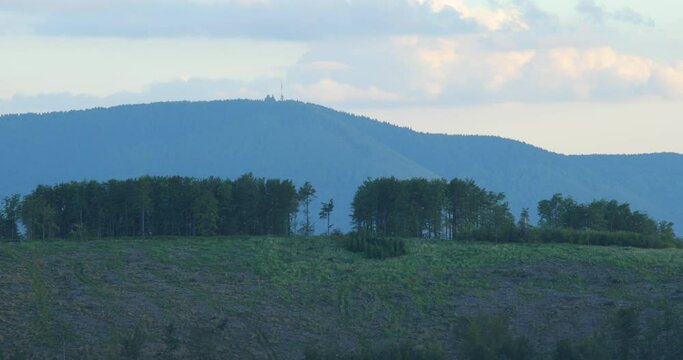 The top of the hill with trees and in the background you can see a mountain with a transmitter on its top Radhost area of Beskydy.