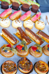 Sweets-tartlets with fruit jelly and fruit slices:strawberries, blueberries, physalis berries, eclairs with chocolate, fountain. Cakes are made by hand by pastry chefs. For sale at a street fair