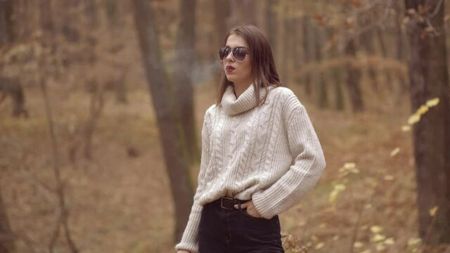 Autumn vogue. Young stylish hipster girl wearing modern dress in urban park and smoking. Caucasian female model. Fall fashion. Woman Smok a Cigarette.
