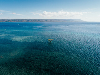 Aerial view of blue sea with a small mangrove tree in the midle of water and a big island on the end