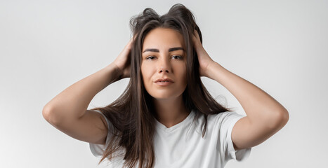 Fototapeta premium Pretty carefree modern girl with long chestnut hair holding to her head or touching hair. Isolated on white background. Emotions, expressions, hairstyle and people concept.