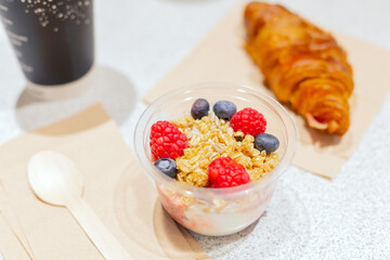 Jar of yogurt, jam, muesli, blueberries, raspberries a croissant, a Cup of coffee with you. Next to it is a spoon made of natural wood. Healthy ready-made Breakfast at the airport