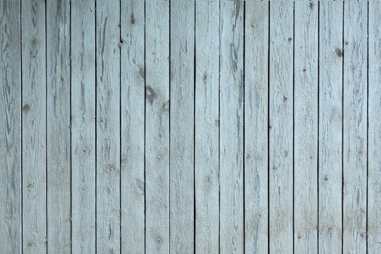 A wooden wall made of rough planks arranged vertically. The old light paint has partially collapsed, and the wood texture is visible. Background.