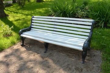 White bench in the park against the background of green bushes.