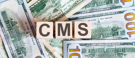 Concept words CMS on wooden blocks on a beautiful background from dollar bills.