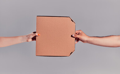 Close-up image of courier hands delivering pizza to customer isolated on gray background.