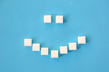 White sugar cubes laid out in the form of a smile on a blue background close-up. Concept of health, dentistry