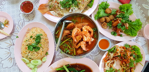 Flat lay of Thai food with fried rice, spicy salad, steamed fish and Sour soup with shrimp and mixed vegetables on the dining table. Top view of Asian food with spicy and sweet sauce.