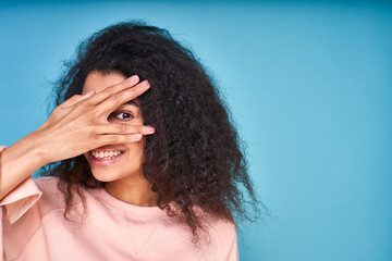 A young dark-skinned woman with curly hair looks through her fingers.