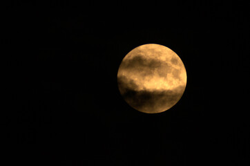 Luna piena immersa nel buio con nuvole in transito.