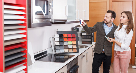 Young couple looking material for kitchen furniture in salon