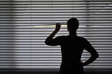 Suspicious woman looking outside through a venetian curtain blinds