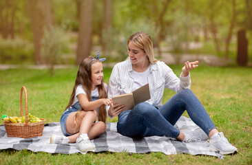 Positive Mother And Daughter Reading And Discussing Book In Park