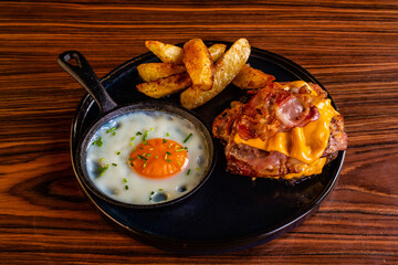 Hamburger con bacon, cheddar, contorno di patate al forno e uovo cotto all'occhio di bue