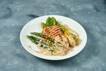 Grilled turkey steak with asparagus and sauce in white plate on gray background