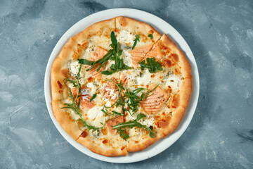 Appetizing cheese pizza with salmon and arugula in a white plate on a gray background. Top view. Seafood pizza