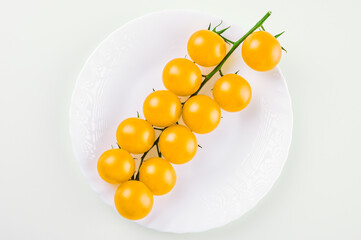 a branch of yellow small tomatoes on a white plate