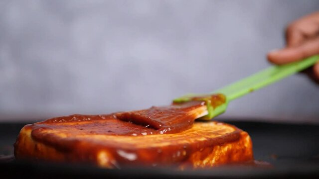Slow motion closeup of barbecue sauce being rubbed on a cottage cheese steak with a brush