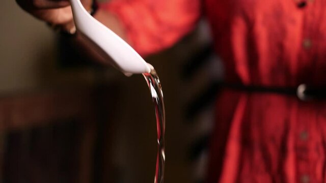 Slow motion closeup of a female cook pouring cooking oil into a pan with a spoon